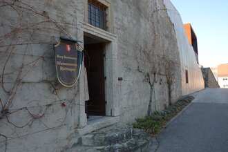 Blick auf den äußeren Eingangsbereich des Weinmuseums in Röttingen. An der Wand hängt ein großes Ritter-Schutzschild mit der Aufschrift "Burg Brattenstein, Weinmuseum Röttingen" . | © Stadt Röttingen