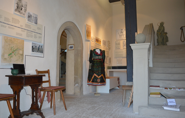 Blick in den Innenbereich des Weinmuseums in Röttingen. Hier ist eine Tracht sowie ein alter Sekretär mit Stühlen zu sehen. Eine Treppe führt in die zweite Etage. | © Stadt Röttingen