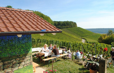 Ein Gruppe von 3 Personen sitzt auf einer Biergartengarnitur vor einem Weinberghäuschen direkt in den Weinbergen. Das Bild zeigt den Weinausschank im Weinberghäusle. | © Tourismus im Weinsberger Tal e.V.