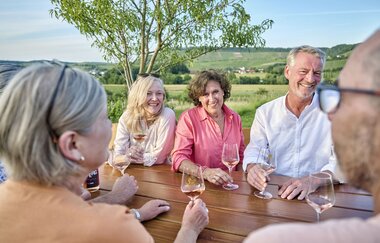 Eine gemischte Gruppe sitzt an einem Tisch mit Weingläsern in der Sonne. | © Touristikgemeinschaft HeilbronnerLand