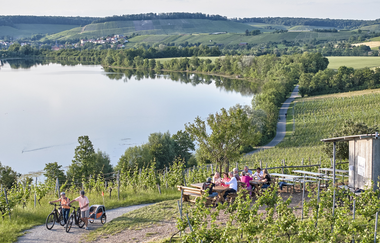 Drohnenaufnahme vom Weinausschank am Breitenauer See. Ein Pärchen mit Fahrrädern kommt geraden den Weinbergweg hinauf. | © Touristikgemeinschaft HeilbronnerLand