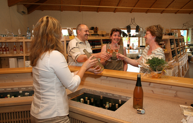 Vier Personen stehen an der Theke und halten Gläser mit Wein und Sekt. Eine Person schenkt mit einer Flasche ein. | © Winzer von Baden