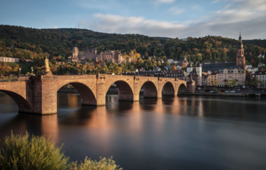 Blick auf das Schloss Heidelberg. Im Vordergrund ist der Neckar und die historische Brücke führt auf die andere Uferseite. Das Schloss ist am Berg gelegen. Hinter dem Schloss befindet sich ein dunkelgrüner Wald. Vor dem Schloss ist die Stadt zu erkennen. | © SSG, Foto: Günther Bayerl