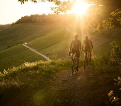 Mann und Frau gravelbiken über die Höhenzüge des Kraichgau-Strombergs. Im Hintergrund Sonnenuntergang. | © Tourimia Tourismus GmbH | Stefan Leitner Photography