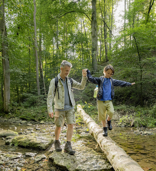 Junge balanciert auf einem Holzstamm über die Schmerach | © Hohenlohe + Schwäbisch Hall Tourismus e. V.