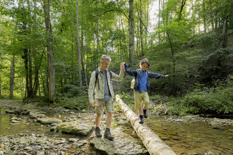 Junge balanciert auf einem Holzstamm über die Schmerach | © Hohenlohe + Schwäbisch Hall Tourismus e. V.