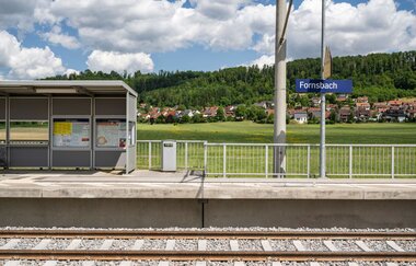 Bahhofgleis in Fornsbach mit grüner Landschaft und Häusern im Hintergrund.