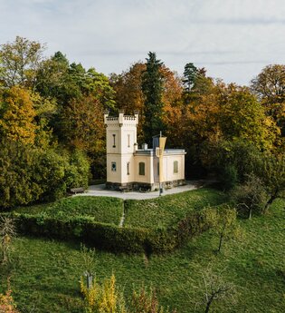 Eine kleine Villa mit Turm steht auf einem grünen Hügel, umgeben von herbstlich bunten Bäumen. | © Stadtverwaltung Crailsheim
