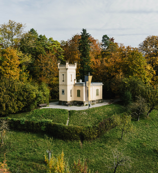 Eine kleine Villa mit Turm steht auf einem grünen Hügel, umgeben von herbstlich bunten Bäumen. | © Stadtverwaltung Crailsheim