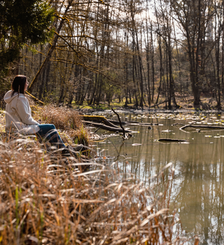 Eine Frau sitzt in einem See, der umrandet ist von Bäumen und Schilf | © Stadtverwaltung Crailsheim