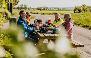 Eine Gruppe Radfahrer sitzen auf einer Bank mit Tisch und unterhalten sich lächelnd | © Stadtverwaltung Crailsheim