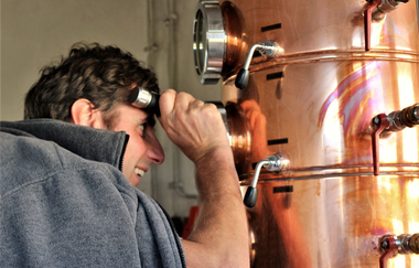 Ein Mann schaut während des Brennvorgangs in einen Kupferkessel | © Touristikgemeinschaft Hohenlohe e. V. | Jürgen Koch