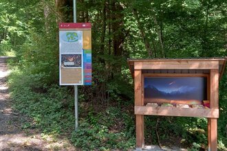 bunte Infotafel am Gaildorfer Geopfad, daneben Wurfbude mit Dinosauriern