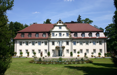 Das Schloss ist außen weiß und hat an der Fassade Rehgeweihe hängen. Es ist von einem Park umgeben. | © Touristikgemeinschaft Hohenlohe e. V. | Wald & Schlosshotel Friedrichsruhe