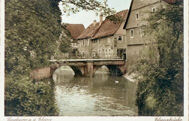 historische Aufnahme verschiedener Gebäude an einem Fluss mit Brücke