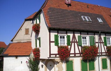 Fachwerkhaus mit Blumenschmuck und grünen Fensterläden unter Sommerhimmel