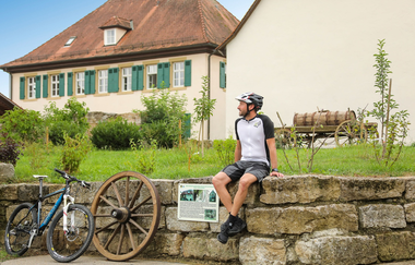 Ein Radfahrer sitzt auf einer Mauer | © Touristikgemeinschaft Hohenlohe e. V. | Andi Schmid, Fotolevel