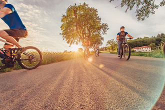 4 Radfahrer fahren auf einem asphaltierten Radweg bei Sonnenuntergang. Im Hintergrund ist Wald und ein Haus zu sehen. | © Touristikgemeinschaft Odenwald e.V.