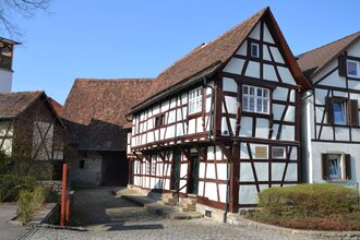 Ein Fachwerkhaus mit weißem Putz und braunen Holzbalken, Steindach und gepflastertem Hof | © Stadt Sinsheim