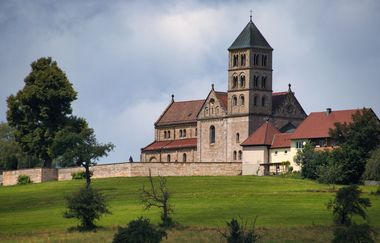 Romanische Kirche auf Hügel umgeben von Mauer. Grüne Wiesen und Bäume. | © Hohenlohe Schwäbisch Hall