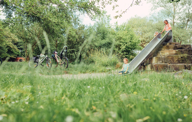 Drei Mädchen spielen an einer Rutsche, am linken Bildrand sind zwei Fahrräder zu sehen. | © Touristikgemeinschaft HeilbronnerLand