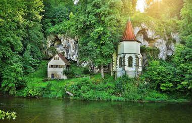 Die Wallfahrtskapelle steht am Fluss Jagst mit einer aufragenden Tuffsteinfelsenwand dahinter | © Touristikgemeinschaft Hohenlohe e. V. | Andi Schmid