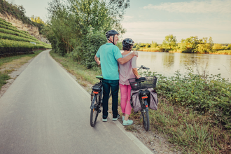 Ein Mann und eine Frau mit Fahrrädern stehen am Fluss. | © Touristikgemeinschaft HeilbronnerLand