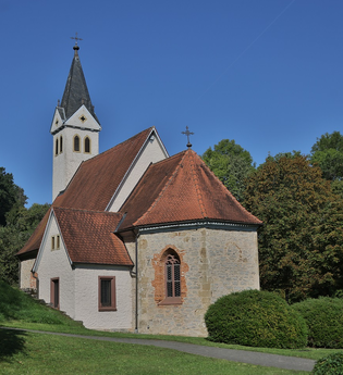 Die Kirche hat einen spitzen Turm und ist von grünen Bäumen umgeben | © Touristikgemeinschaft Hohenlohe e. V. | Andi Schmid
