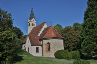 Die Kirche hat einen spitzen Turm und ist von grünen Bäumen umgeben | © Touristikgemeinschaft Hohenlohe e. V. | Andi Schmid