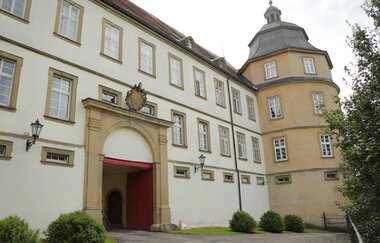 Das Schloss hat einen Turm und ein Wappen über dem weißen Eingang | © Touristikgemeinschaft Hohenlohe e. V.