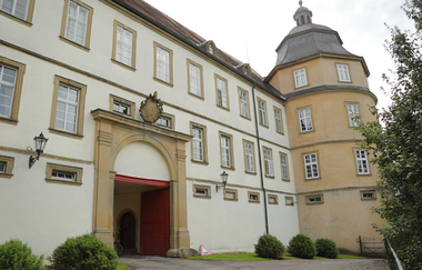 Das Schloss hat einen Turm und ein Wappen über dem weißen Eingang | © Touristikgemeinschaft Hohenlohe e. V.