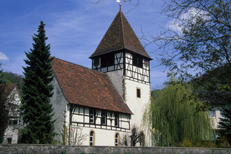 Die Kirche hat Fachwerk rund ums Gebäude und ist von Bäumen umgeben | © Touristikgemeinschaft Hohenlohe e. V. | Eva Maria Kraiss
