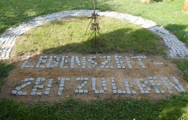 Ein Halbkreis mit dem mit Pflastersteinen gelegten Schriftzug Lebenszeit - Zeit zu Leben | © Touristikgemeinschaft Hohenlohe e. V. | Evangelische Kirchengemeinde Crispenhofen-Weißbach
