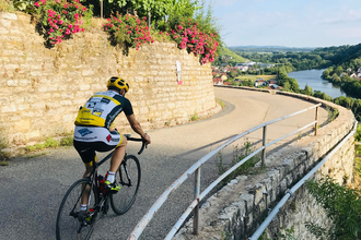 Ein Rennradfahrer fährt auf einer kurvigen Straße oberhalb des Neckars entlang – umgeben von Trockenmauern, Weinreben und weitem Ausblick über das Neckartal. | © Kraichgau-Stromberg Tourismus e.V.
