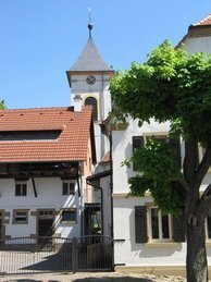 Weißer Kirchturm mit Uhr hinter Häusern unter blauem Himmel | © Stadt Sinsheim