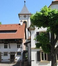 Weißer Kirchturm mit Uhr hinter Häusern unter blauem Himmel | © Stadt Sinsheim