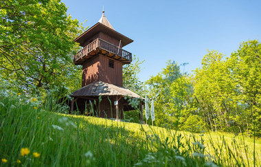 hölzerner Aussichtsturm  mit Turmumlauf  vor hellgrünen Laubbäumen, im Vordergrund eine Wiese mit gelben und weißen Blumen, an einem sonnigen Frühlingstag | © Stadt Gaildorf