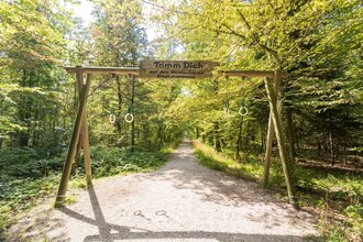 Hölzernes Sportgerät im Wald mit dem Schild ,,Trimm dich" | © Stadtverwaltung Crailsheim