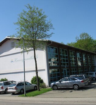 Weiße Veranstaltungshalle mit großer Fensterfront mit parkenden Fahrzeugen | © Stadt Sinsheim