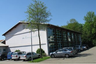 Weiße Veranstaltungshalle mit großer Fensterfront mit parkenden Fahrzeugen | © Stadt Sinsheim