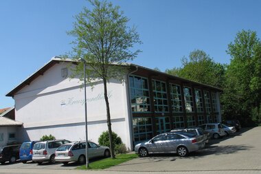 Weiße Veranstaltungshalle mit großer Fensterfront mit parkenden Fahrzeugen | © Stadt Sinsheim