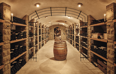 eleganter Gewölbekeller mit mehreren, gut bestückten, Weinregalen rechts und links. In der Mitte des Kellers steht ein Weinfass | © Weingut Albrecht-Kiessling