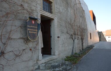 Blick auf den äußeren Eingangsbereich des Weinmuseums in Röttingen. An der Wand hängt ein großes Ritter-Schutzschild mit der Aufschrift "Burg Brattenstein, Weinmuseum Röttingen" . | © Stadt Röttingen