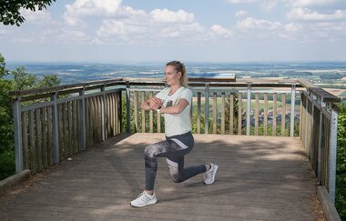 Eine Sportlerin macht eine Kniebeuge auf einer Aussichtsplattform | © Touristikgemeinschaft Hohenlohe e. V. | Fa. Würth
