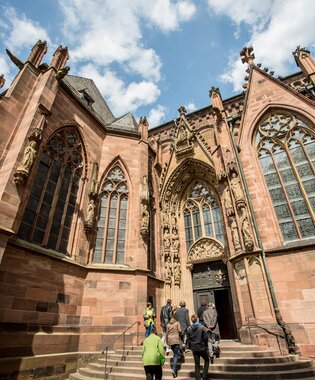 Das Südportal des Wormser Doms mit gotischen Spitzbogenfenstern, steinernen Figuren und mehreren Personen, die die Stufen hinauf zum Eingang gehen | © Worms Touristik, Foto Bernward Bertram 