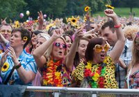 Menschenmenge bei einer Open-Air-Veranstaltung mit Sonnenblumen und bunten Blumenketten, einige heben die Arme | © Foto: Bernhardt Kreutzner