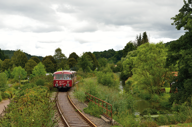 Roter Zug fährt auf Gleisen durch grünes Tal. | © Krebsbachtalbahn; Frank Jennerwein
